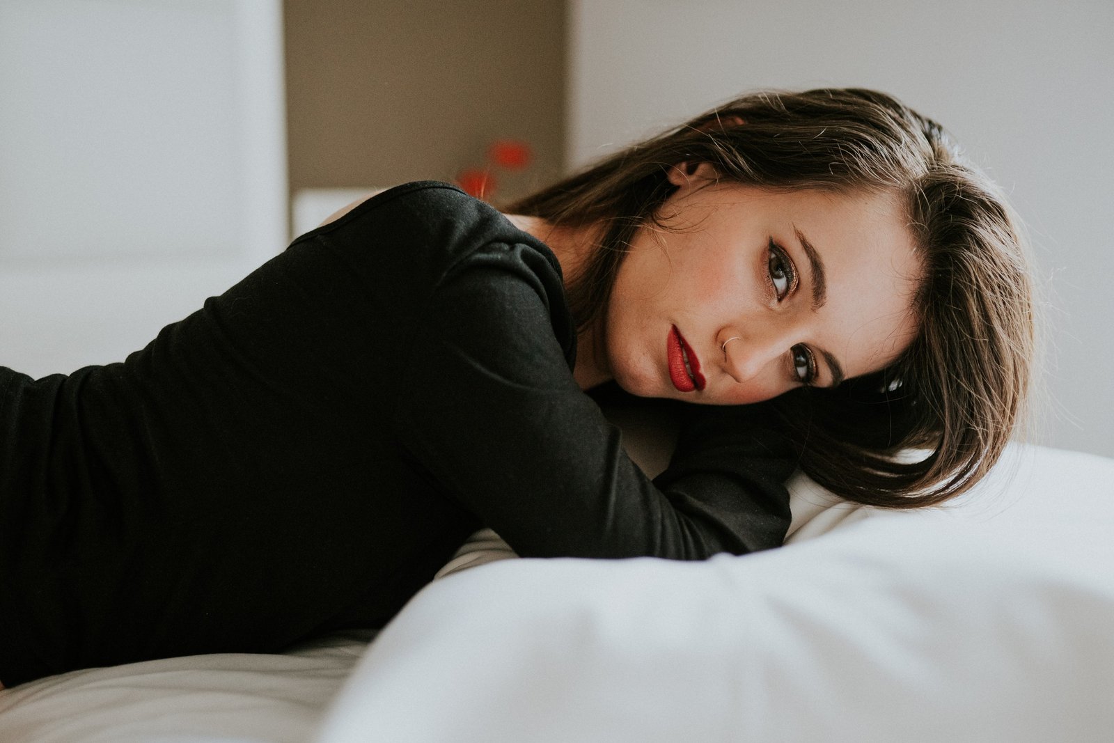 Mujer tumbada en una cama con un jersey negro de manga larga, apoyando la cabeza en los antebrazos y mirando a cámara con una sonrisa sutil. Fotografía de boudoir de Víctor Ruiz, Granada.
